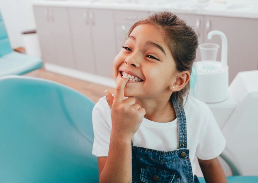 Little girl pointing to smile during her children's dentistry visit