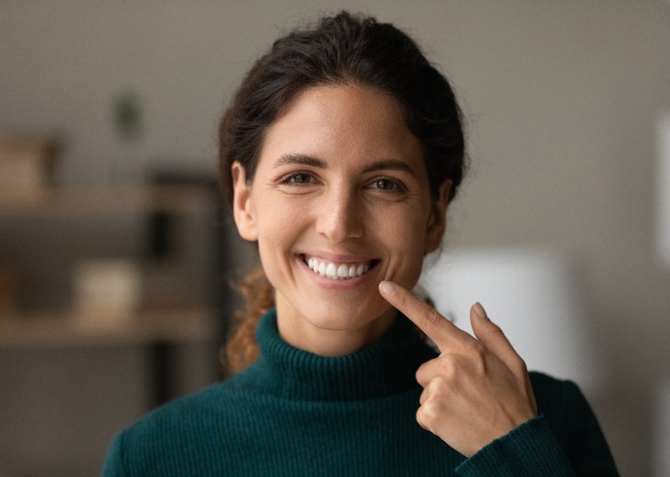 Woman in dark green sweater pointing to smile
