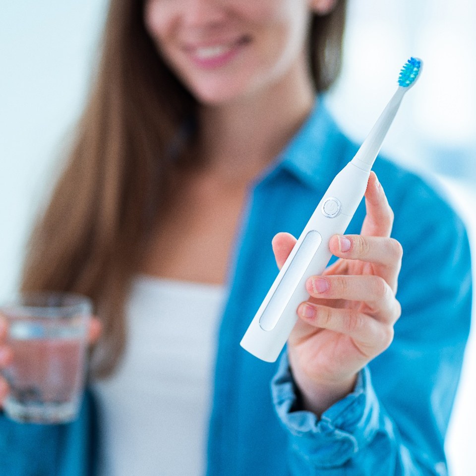 Woman with blue jacket holding an electric toothbrush