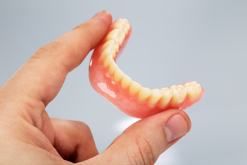 A hand holding a loose lower denture