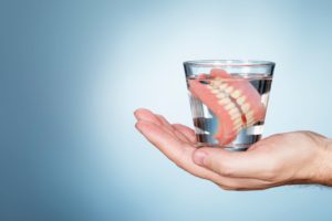 A hand holding a glass of water containing dentures