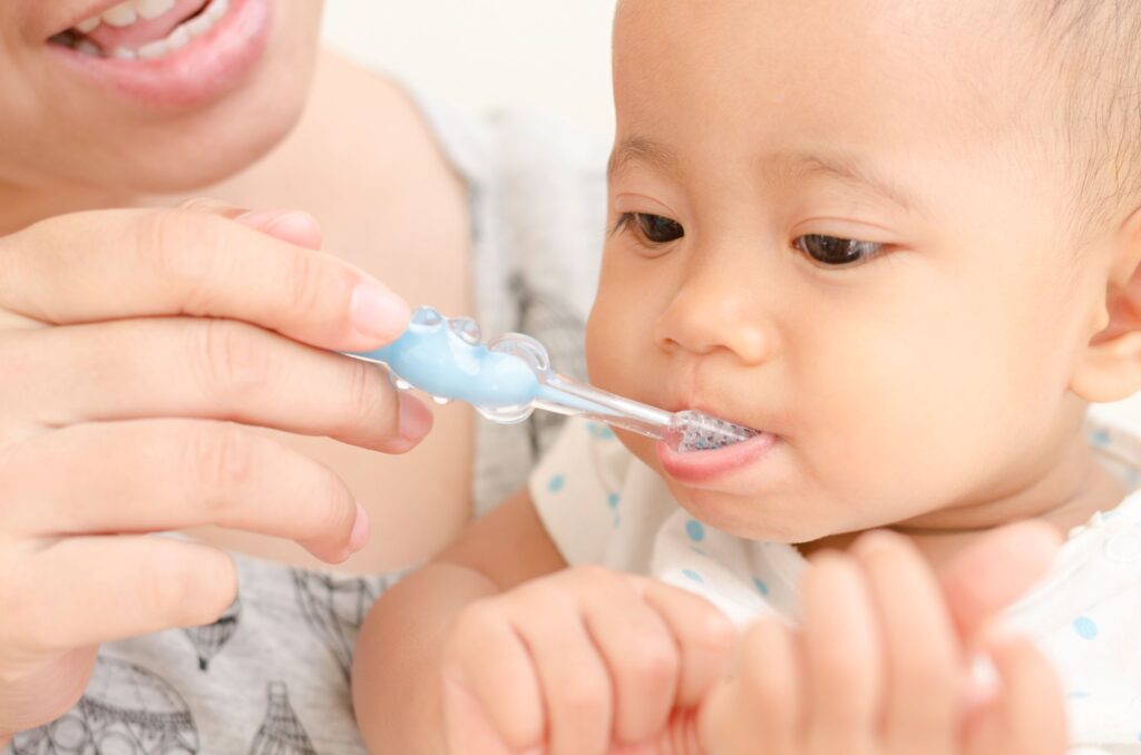 Woman holding blue, child-sized toothbrush to baby's mouth